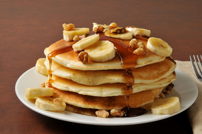 Pile of pancakes with banana and maple syrup on its top